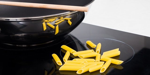 Frying pan, sticks and pasta in modern kitchen with induction stove