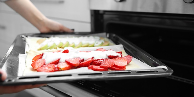 Female hands placing strawberry and apple desserts into oven